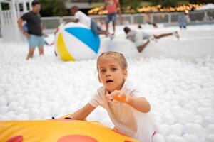 contento poco ragazza giocando bianca plastica palle piscina nel divertimento parco. terreno di gioco per bambini. foto