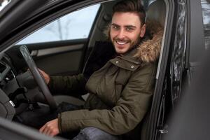 giovane attraente caucasico uomo si siede a il ruota di il suo auto soleggiato inverno giorno. foto