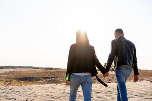 giovane europeo coppia vestito pelle giacca e blu jeans a piedi deserto Tenere mani Visualizza a partire dal il Indietro. foto