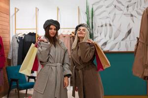 Due donne amiche nel un' moda boutique scegliere un' cappotto per autunno stagione. foto