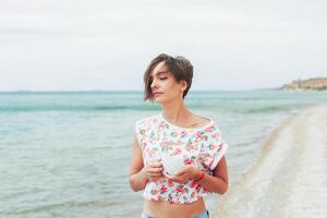 bellissimo donna rilassare durante esotico vacanza su il spiaggia godendo dolce caffè foto