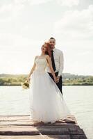 nozze coppia a piedi su ponte vicino lago su tramonto a nozze giorno. sposa e sposo nel amore foto