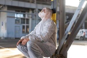 disperazione assistenza sanitaria lavoratore nel bianca covid protettivo tuta da lavoro. stanco maschio caucasico medico nel depressione durante coronavirus pandemia foto