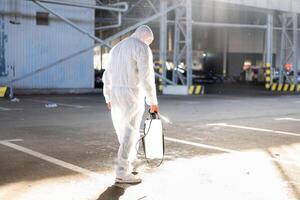 uomo vestito bianca protettivo tuta da lavoro spruzzatura superficie antibatterico disinfettante spruzzatore durante quarantena foto