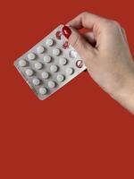 avvicinamento Visualizza di bolla imballare con pillole nel femmina mano isolato su rosso sfondo foto
