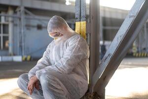 disperazione assistenza sanitaria lavoratore nel bianca covid protettivo tuta da lavoro. stanco maschio caucasico medico nel depressione durante coronavirus pandemia foto