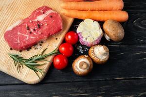 uno pezzi di succoso crudo Manzo con verdure su un' taglio tavola su un' nero di legno tavolo sfondo. foto