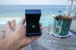 mano Tenere un' scatola con Fidanzamento squillare con oceano Visualizza sfondo. foto