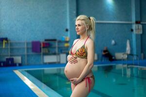 incinta donna in piedi in casa nuoto piscina abbraccio grande pancia foto