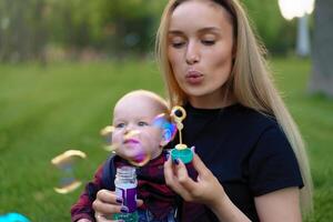 giovane caucasico madre si gonfia sapone bolle con sua poco figlio nel un' parco su un' soleggiato estate giorno. foto