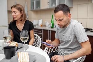 amici incontro con vino e torta nel il moderno stile cucina. giovane donna Sorridi e scherzo. il uomo è focalizzata su un' mobile Telefono foto