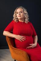 incinta donna in posa nel un elegante rosso vestito in casa studio nero parete sfondo foto