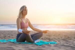 donna pratica yoga loto posa per meditazione con estate vacanza spiaggia felicità e rilassamento. calma femmina esercizio con yoga meditare oceano spiaggia con tramonto d'oro volta. foto