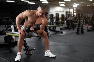 muscolare atletico bodybuilder fitness modello seduta panchina formazione bicipite sollevamento manubri nel interno Palestra foto