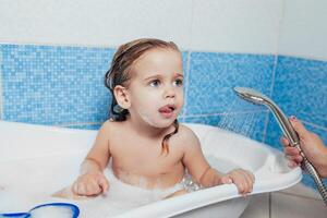 poco bellissimo ragazza bagna nel un' bagno, giochi il scemo e Spettacoli lingua. divertimento bagnarsi bambini. positivo igiene. indipendente bambino foto