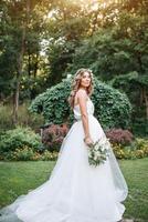 un' carino Riccio donna nel un' bianca nozze vestito con un' nozze mazzo e ghirlanda nel sua capelli in piedi indietro per il telecamera nel natura. concetto sfuggito sposa. inoltrare per un' contento luminosa futuro scappa foto