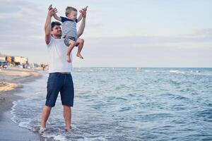 giovane caucasico papà con poco figlio camminare caldo estate giorno lungo il mare costa. estate famiglia vacanza concetto. amicizia padre e figlio. foto