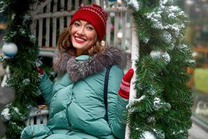 giovane bellissimo caucasico ragazza vestito nel un' caldo inverno giacca, a maglia cappello e guanti si siede su Natale decorato swing all'aperto foto