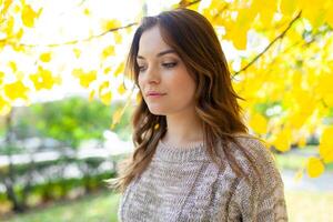 bellissimo caucasico brunetta ragazza in piedi caldo autunno giorno con sfondo di alberi con giallo fogliame foto