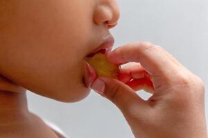 vicino su Visualizza di un' poco asiatico ragazza mangiare un' verde uva foto