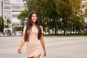 asiatico ragazza nel un' bellissimo aderente beige vestito passeggiate attraverso il città strade e sembra lontano. foto