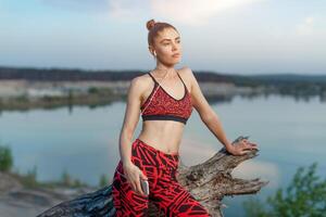 un' bellissimo brunetta ragazza nel elegante gli sport Abiti è riposo dopo un' sport attivo allenarsi vicino il lago. foto