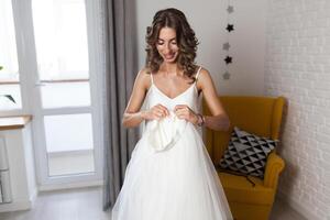 un' bellissimo dai capelli ricci ragazza, un' futuro sposa misurazione un' nozze vestito nel sua Casa prima il nozze. foto