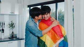 coppia gay asiatica in piedi e abbracciando la stanza a casa. giovani bei uomini lgbtq che si baciano felicemente rilassati riposano insieme trascorrono del tempo romantico in cucina moderna con bandiera arcobaleno a casa al mattino concetto. foto
