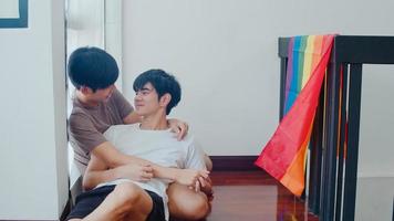 coppia gay asiatica sdraiata e abbracciata sul pavimento a casa. i giovani uomini lgbtq asiatici che si baciano felici si rilassano riposano insieme trascorrono del tempo romantico nel soggiorno con la bandiera arcobaleno nella casa moderna al mattino. foto