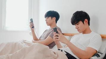 coppia gay asiatica utilizzando il telefono cellulare a casa. i giovani uomini asiatici lgbtq felici si rilassano riposano insieme dopo il risveglio, controllano i social media sdraiati sul letto in camera da letto a casa al mattino concetto. foto