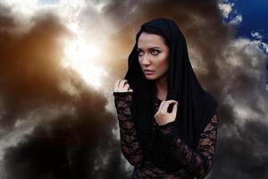 un' donna è un' profeta stregone e un' predicatore nel un' nero mistico mantello con un' cappuccio contro un' drammatico sfondo... foto