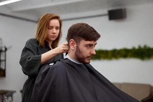 bello blu con gli occhi uomo seduta nel barbiere negozio. parrucchiere parrucchiere donna taglio il suo capelli. femmina barbiere. foto