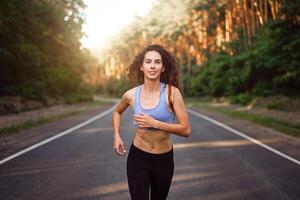 bellissimo caucasico giovane ragazza atleta corre soleggiato estate giorno su asfalto strada nel il foresta. foto