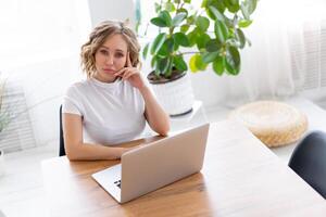 attività commerciale donna utilizzando il computer portatile seduta vicino scrivania bianca ufficio interno con pianta della casa guardare a telecamera foto