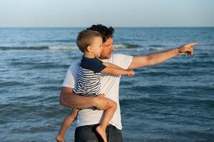 giovane caucasico papà con poco figlio camminare caldo estate giorno lungo il mare costa. estate famiglia vacanza concetto. amicizia padre e figlio. foto