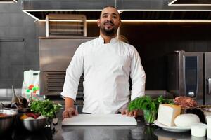 bello giovane africano capocuoco in piedi nel professionale cucina nel ristorante preparazione un' pasto di carne e formaggio verdure. foto