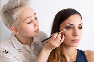 trucco artista l'applicazione luminosa base colore ombretto su Modelli occhio e Tenere un' conchiglia con ombretto su sfondo foto