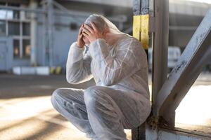 disperazione assistenza sanitaria lavoratore nel bianca covid protettivo tuta da lavoro. stanco maschio caucasico medico afferra il suo testa rannicchiarsi nel depressione durante coronavirus pandemia foto