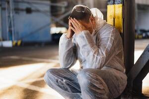 disperazione assistenza sanitaria lavoratore nel bianca covid protettivo tuta da lavoro. stanco maschio caucasico medico afferra il suo testa rannicchiarsi nel depressione durante coronavirus pandemia foto