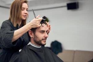 bello blu con gli occhi uomo seduta nel barbiere negozio. parrucchiere parrucchiere donna taglio il suo capelli. femmina barbiere. foto