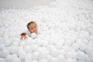 contento poco ragazza giocando bianca plastica palle piscina nel divertimento parco. terreno di gioco per bambini. foto