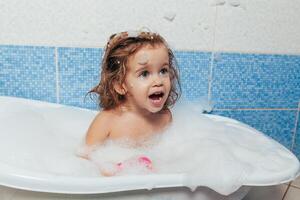 divertimento allegro contento bambino piccolo bambino assunzione un' bagno giocando con schiuma bolle. poco bambino nel un' vasca da bagno. sorridente ragazzo nel bagno su blu sfondo. igiene e Salute cura. foto