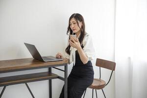 un' giapponese donna controllo smartphone di a distanza opera nel il casa ufficio foto