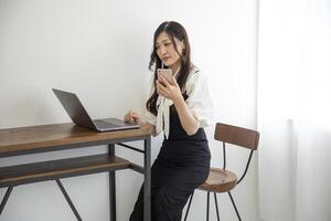 un' giapponese donna controllo smartphone di a distanza opera nel il casa ufficio foto