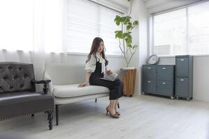 un' giapponese donna controllo smartphone di a distanza opera nel il piccolo ufficio foto