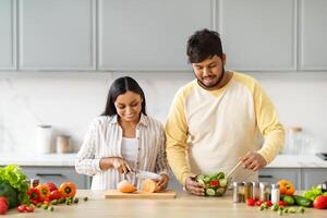 indiano coppia cucinando cibo e sorridente preparazione insalata per cena foto