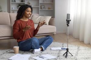 nero femmina divano dando in linea lezione su smartphone telecamera a casa foto