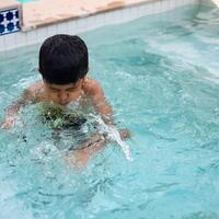 contento indiano ragazzo nuoto nel un' piscina, ragazzo indossare nuoto costume lungo con aria tubo durante caldo estate vacanze, bambini ragazzo nel grande nuoto piscina. foto