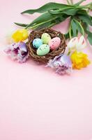 multicolore macchiato uova nel nido con tulipani su rosa sfondo. Pasqua. verticale. copia spazio foto