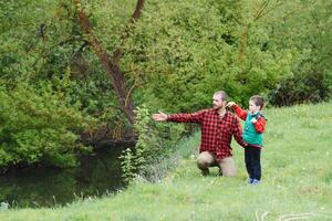 un' padre insegnamento il suo figlio Come per pesce su un' fiume al di fuori nel estate luce del sole foto